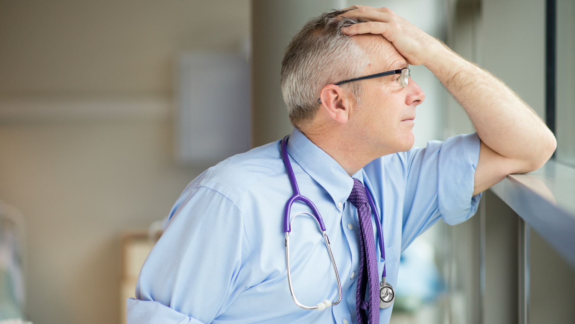 doctor looking out window with hand on his head