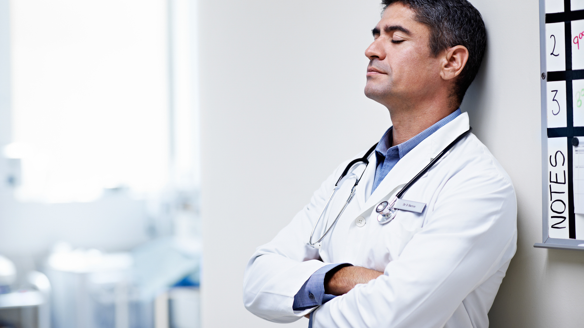 tired male clinician leaning on wall