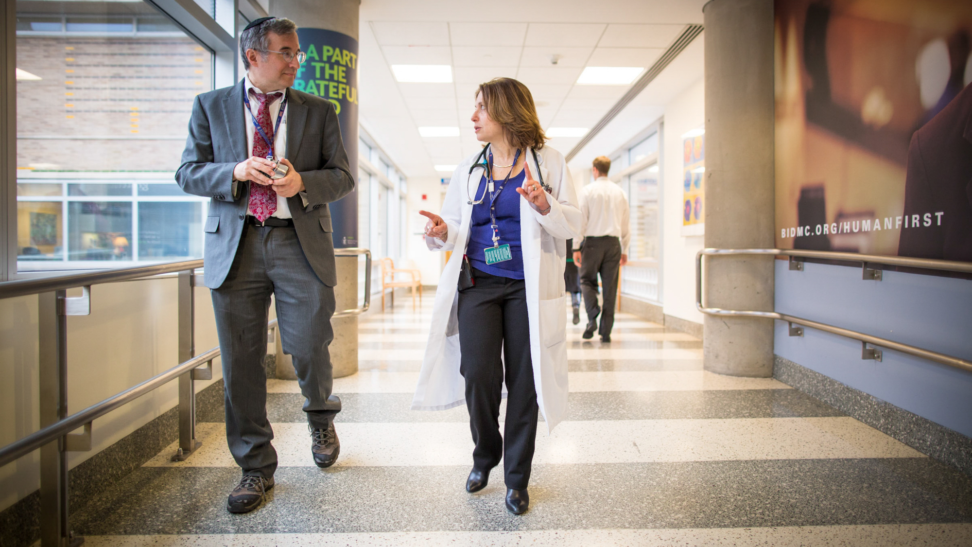 man in a suit and yarmukle and famile clinician discussing something in a hallway