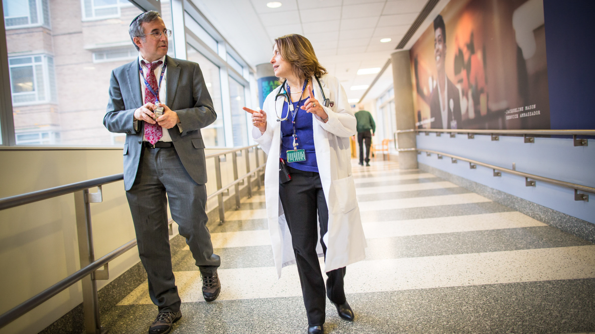 man in a suit and yarmukle and famile clinician discussing something in a hallway