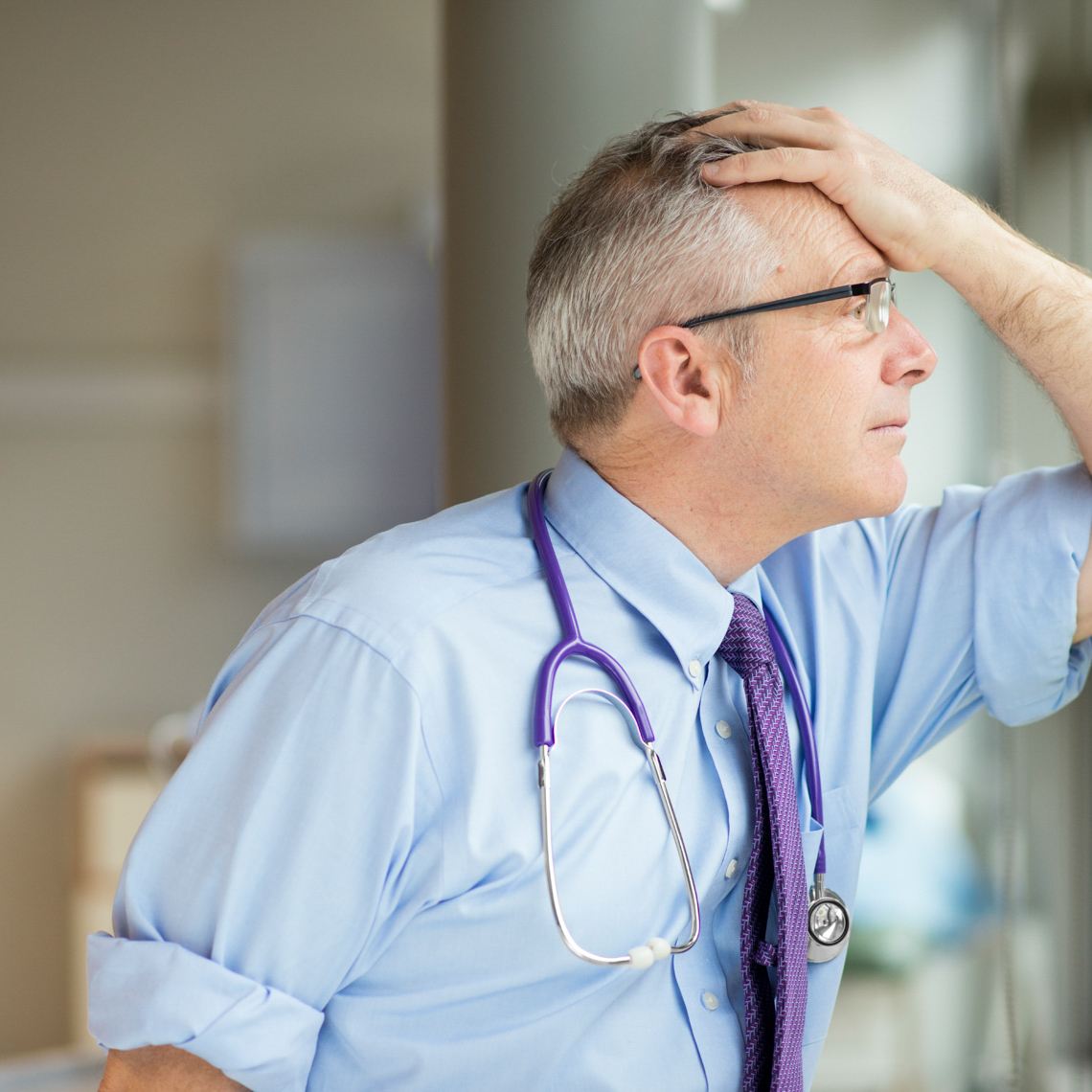 doctor looking out window with hand on his head