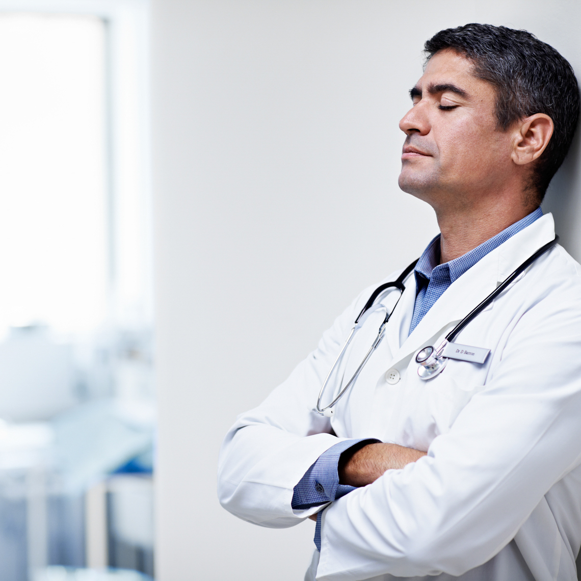 tired male clinician leaning on wall