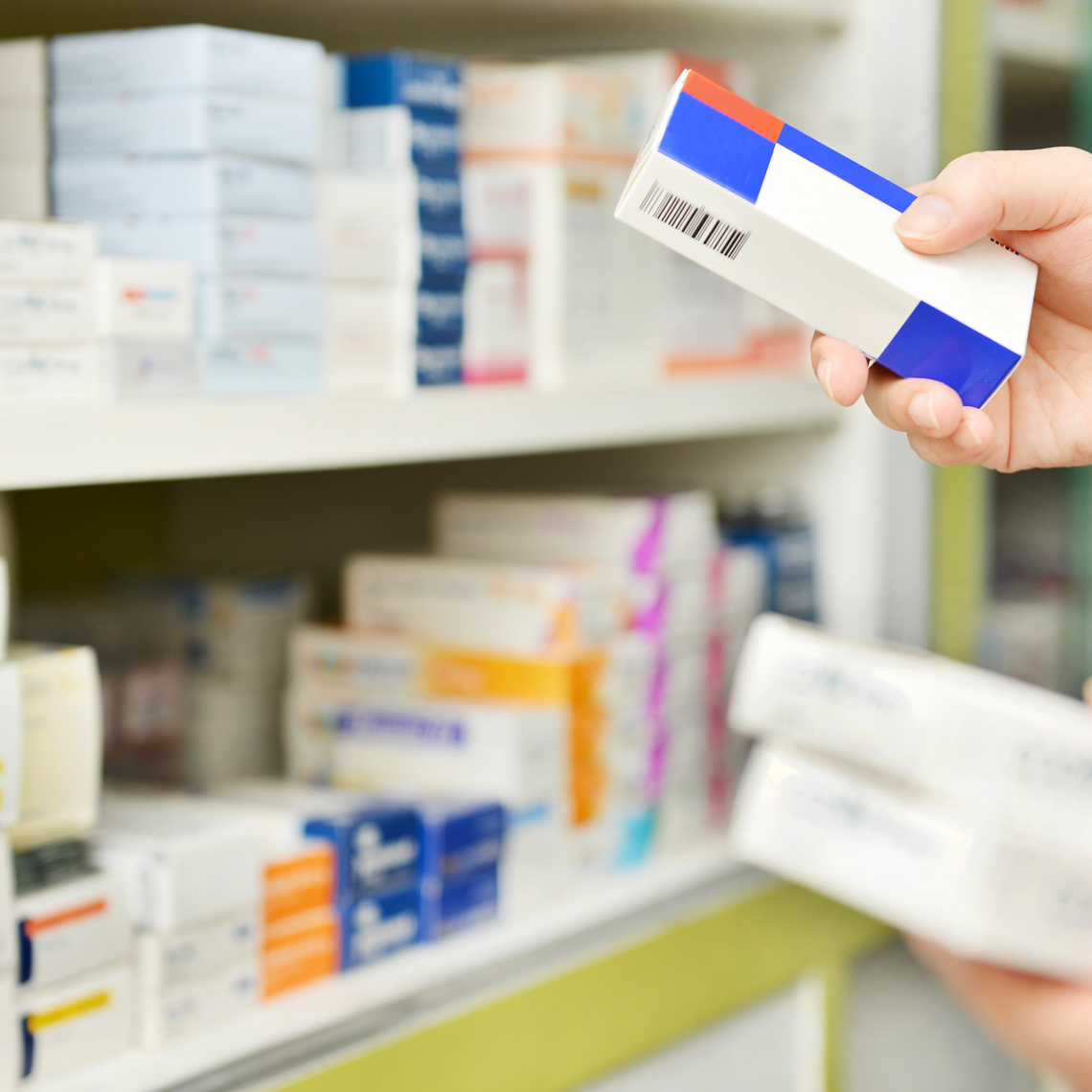 Pharmacist holding medicine box and capsule pack in pharmacy drugstore.