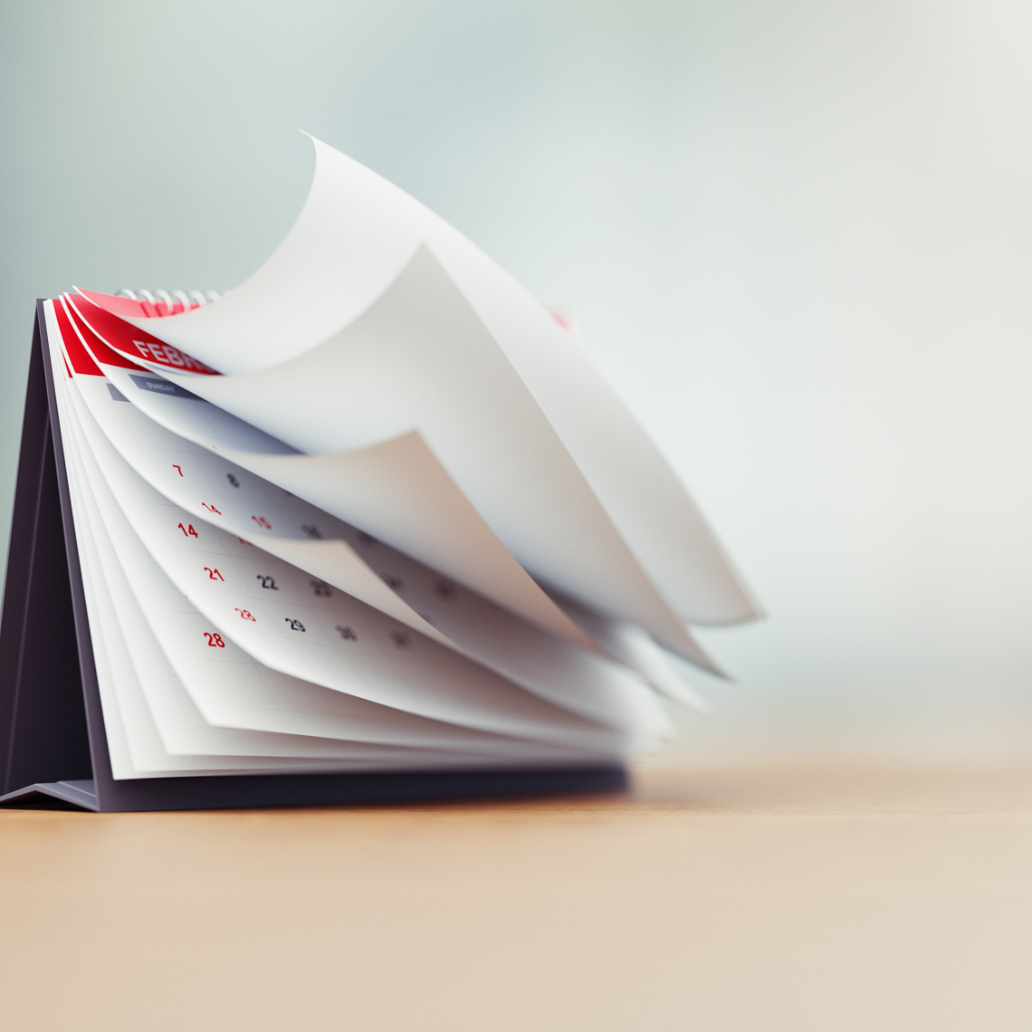 Pages of a red calendar standing over defocused background surface are folding.