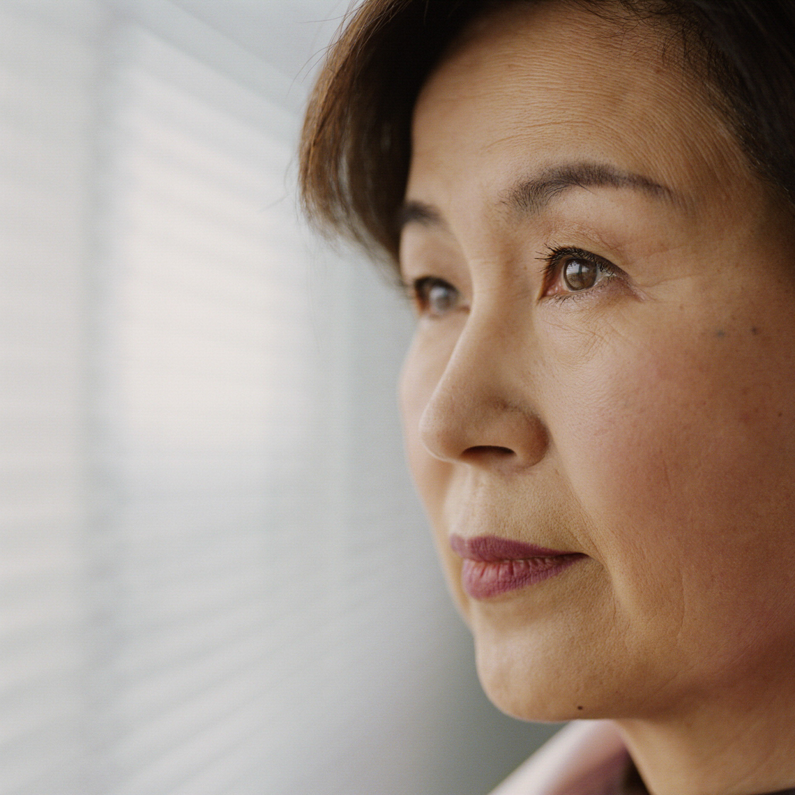 Middle-aged woman of Asian heritage stares thoughtfully out window