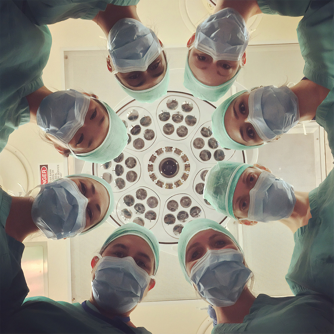 a group of physicians wearing scrubs in an OR looking down at the camera