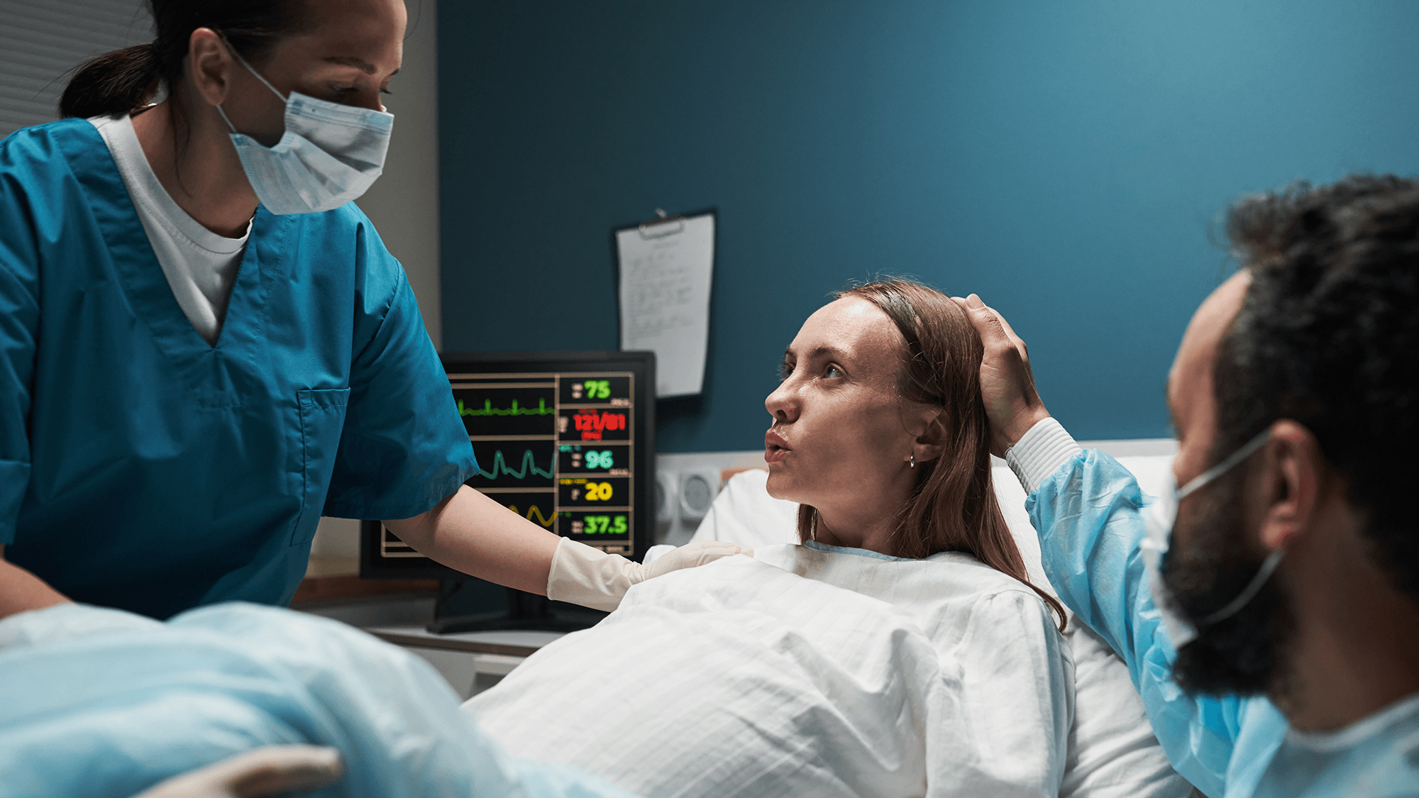 Pregnant female breathing through labor in room with male clinicians in scrubs