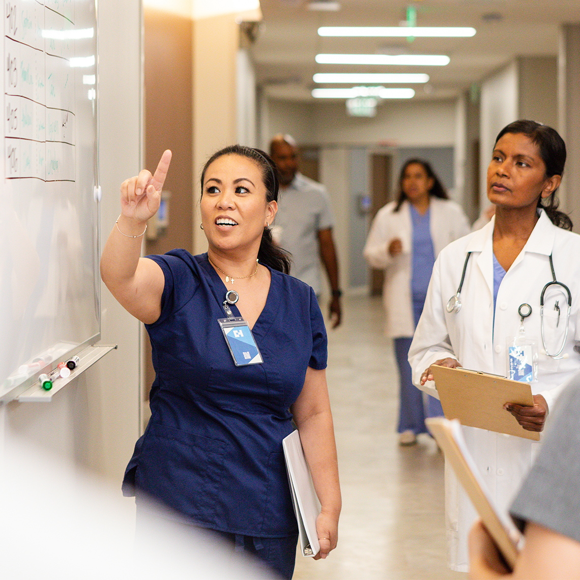 A nurse leads a check-in standing meeting with other clinicians