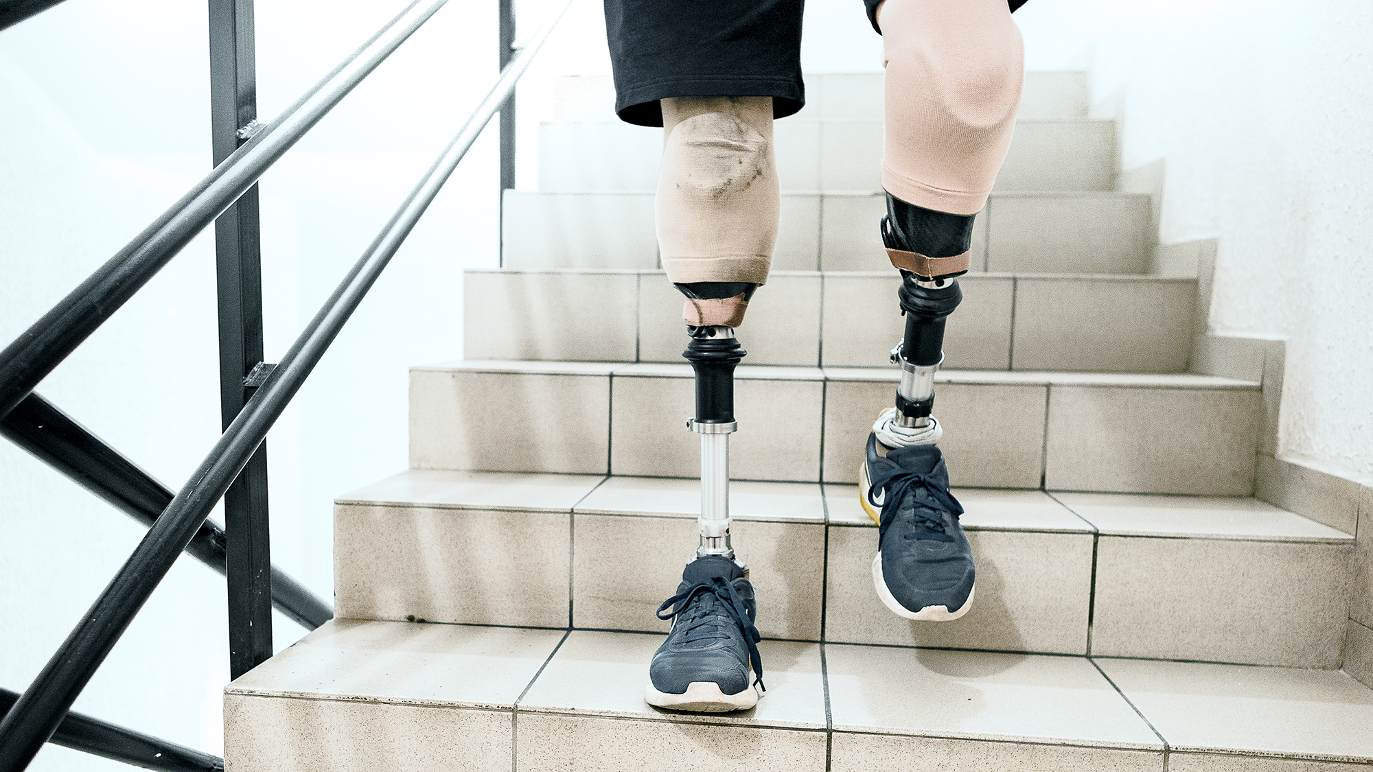 A person seen from the thighs down with two prosthetic legs descending a staircase.