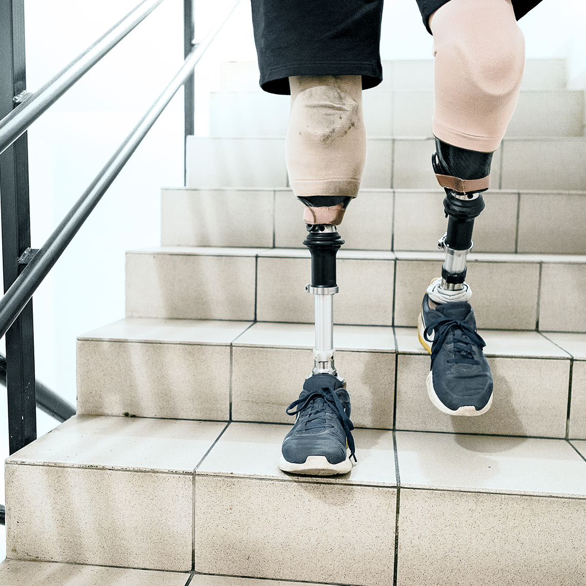A person seen from the thighs down with two prosthetic legs descending a staircase.