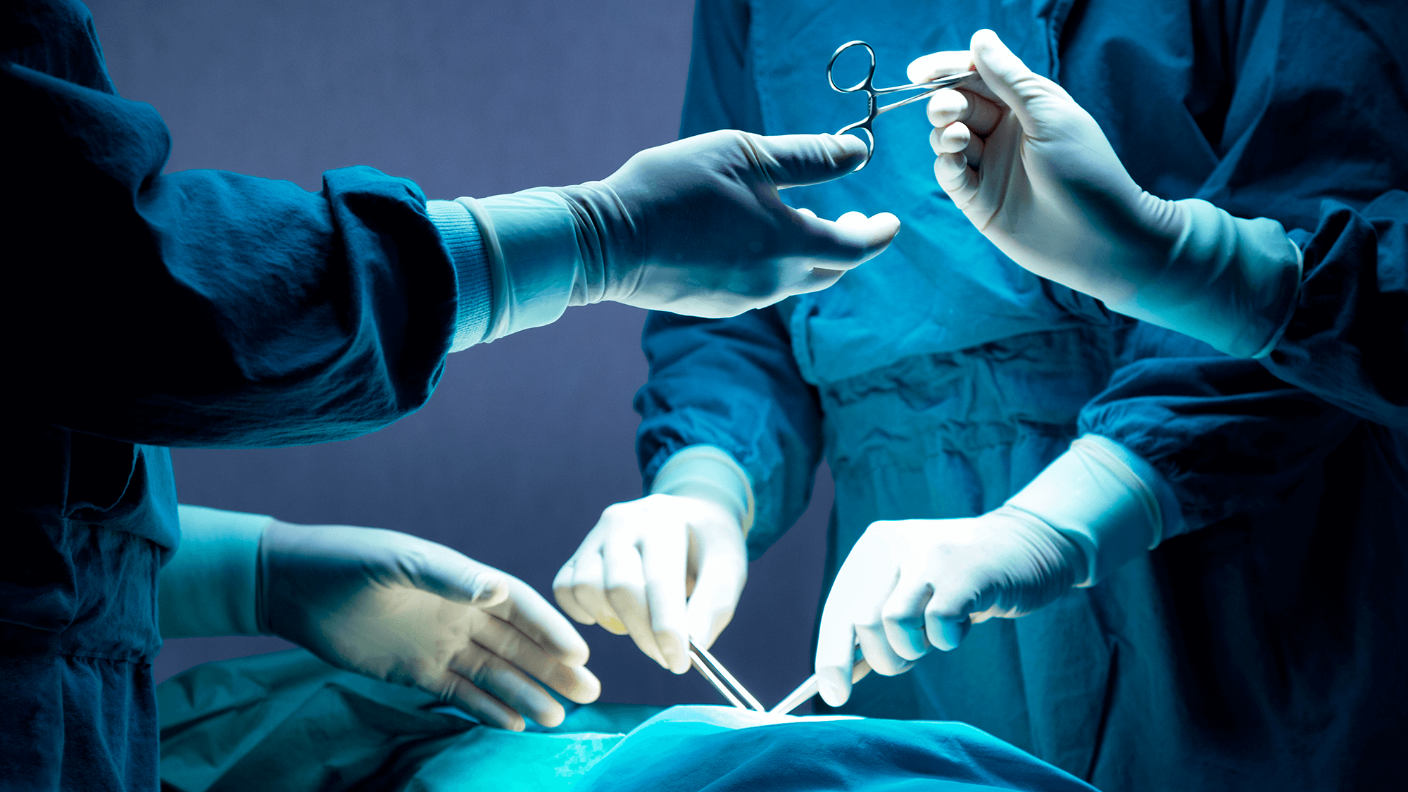 A surgeon conducts a surgical procedure on a patient, with medical equipment and assistants present in the operating theater